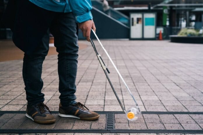 A person uses a tong with a camera and GPS system attached to pick up litter, part of an initiative to boost participation in collecting trash. 