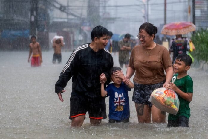 People wade through a flooded road in Balagtas, Bulacan province, Philippines, on July 29, 2023.  