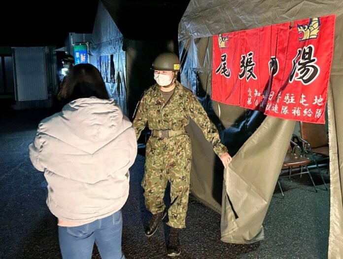 A Ground Self-Defense Force member welcomes a local resident at a bathing facility set up on the grounds of an elementary school serving as an evacuation shelter in Suzu, Ishikawa Prefecture, in March. 